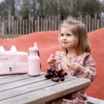 Laps istub laua taga Trixie Pudel Jänes 350 ml roosa joogipudeliga